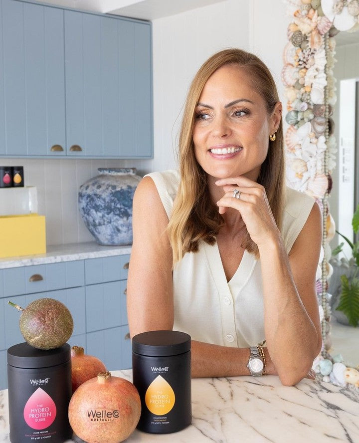 Smiling woman beside fruit and product containers in a bright kitchen.