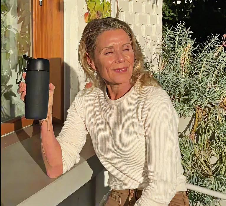 A woman with her eyes closed sits in the sun, holding a black reusable water bottle.